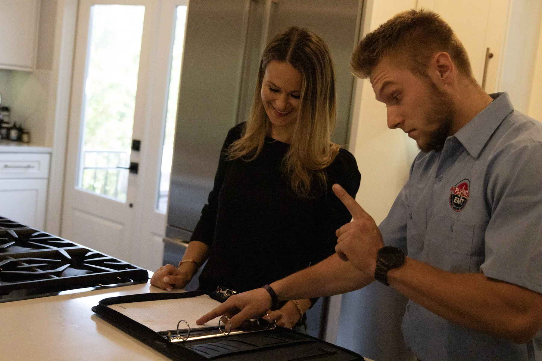 Appliance EMT technician explaining a cooktop fault to a homeowner in her kitchen