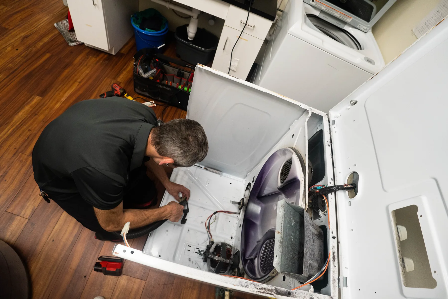 Appliance EMT technician working on an opened dryer in a laundry room