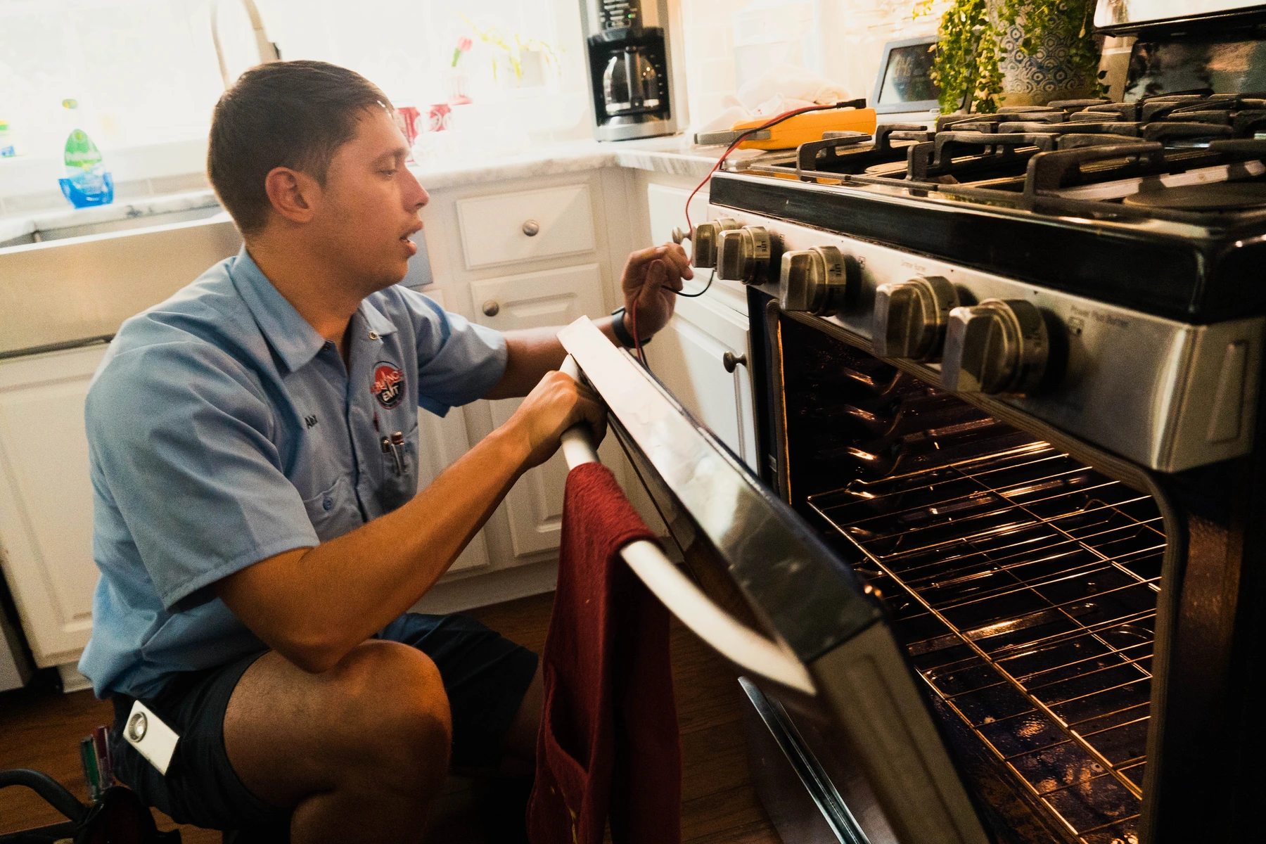 Appliance EMT technician checking the temperature dial on an open oven, interior lit