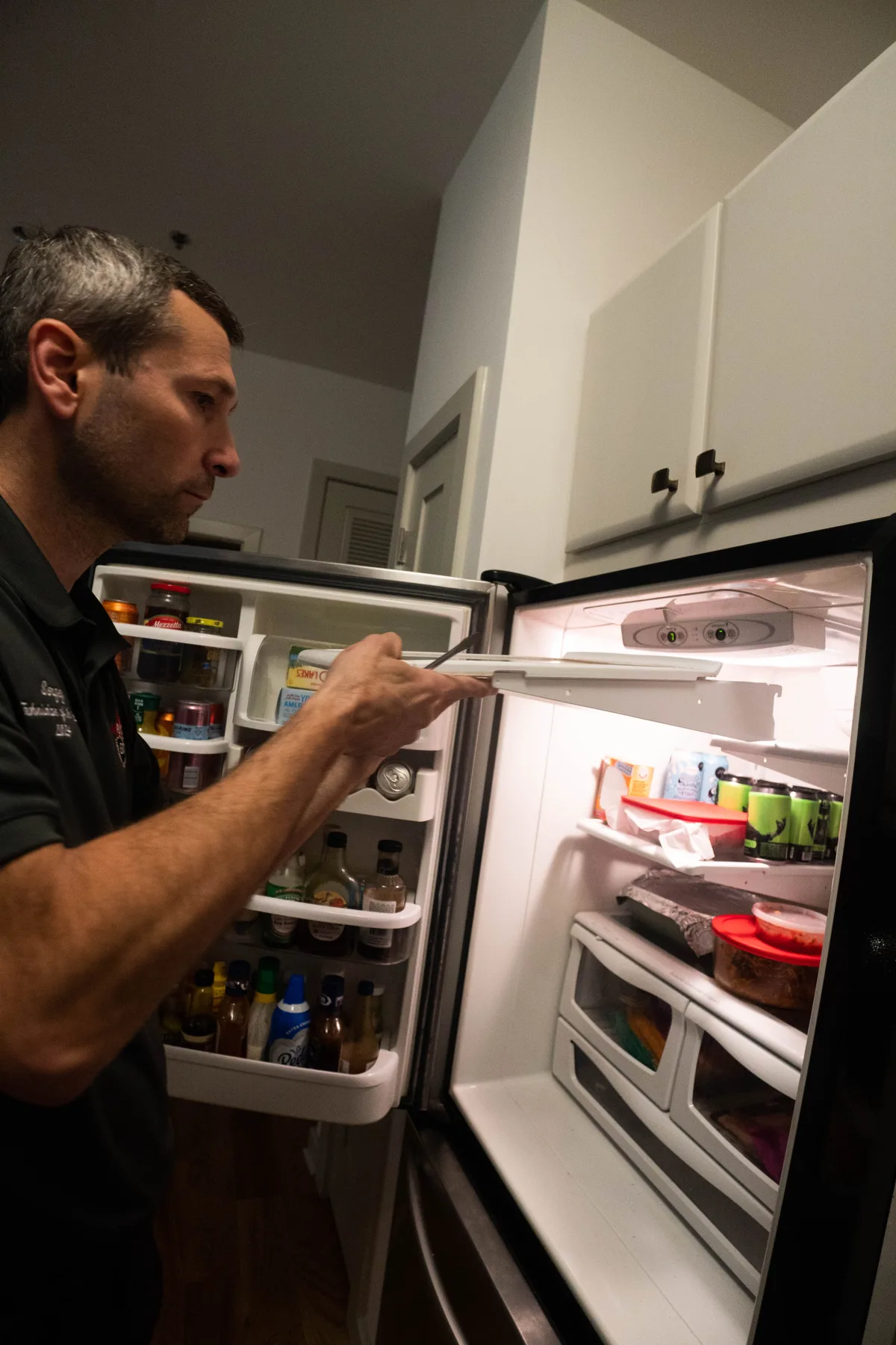 Appliance EMT technician servicing a refrigerator in a customer kitchen